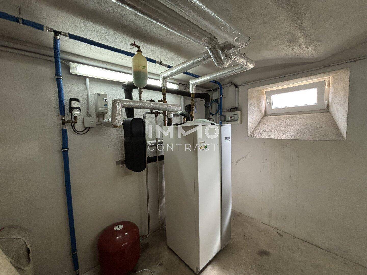 Technikraum mit Heizungsanlage, Rohren und einem kleinen Fenster für Belüftung.