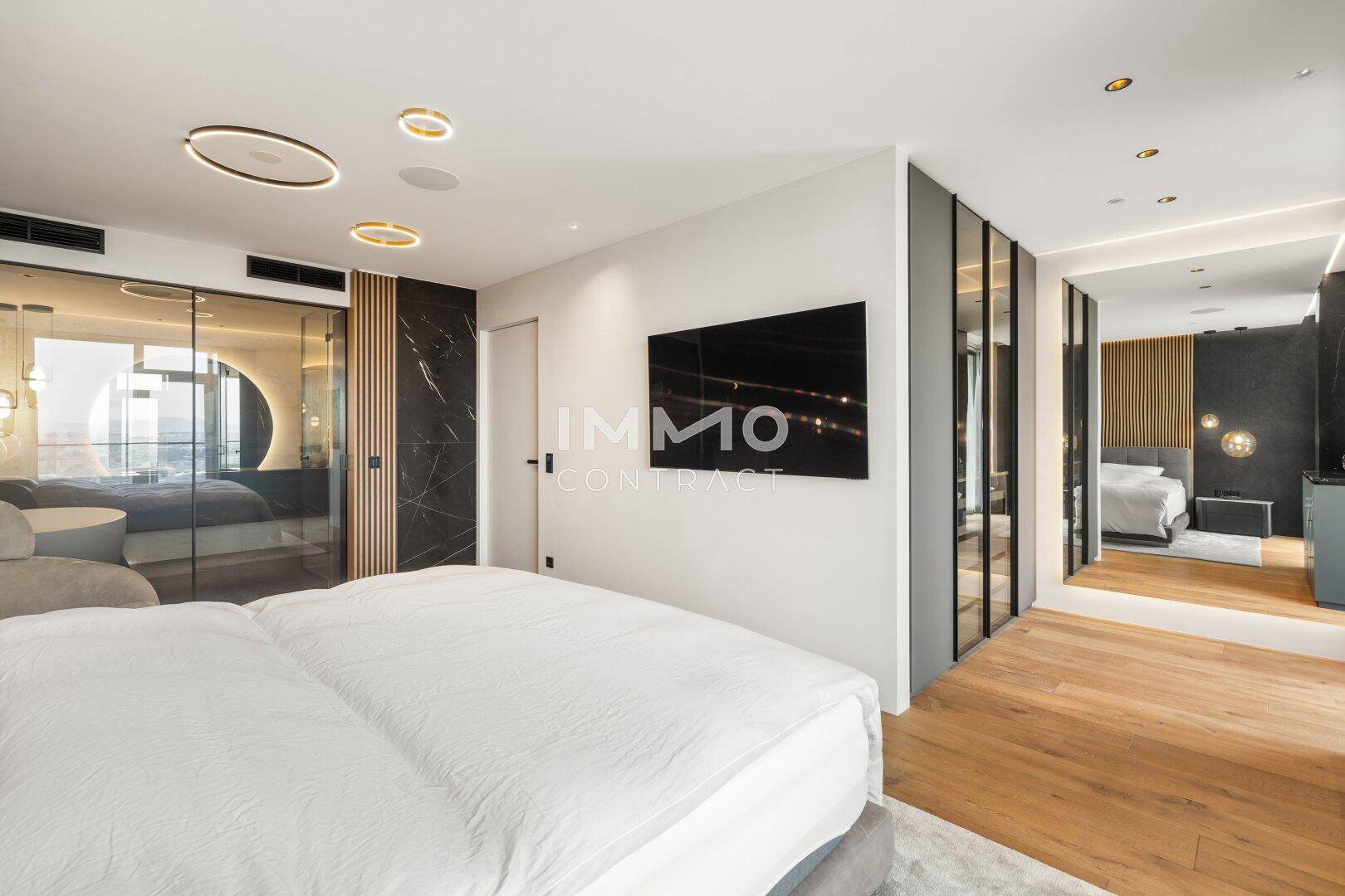 Helles Schlafzimmer mit Holzboden, integriertem TV und Zugang zu einem weiteren Bereich.