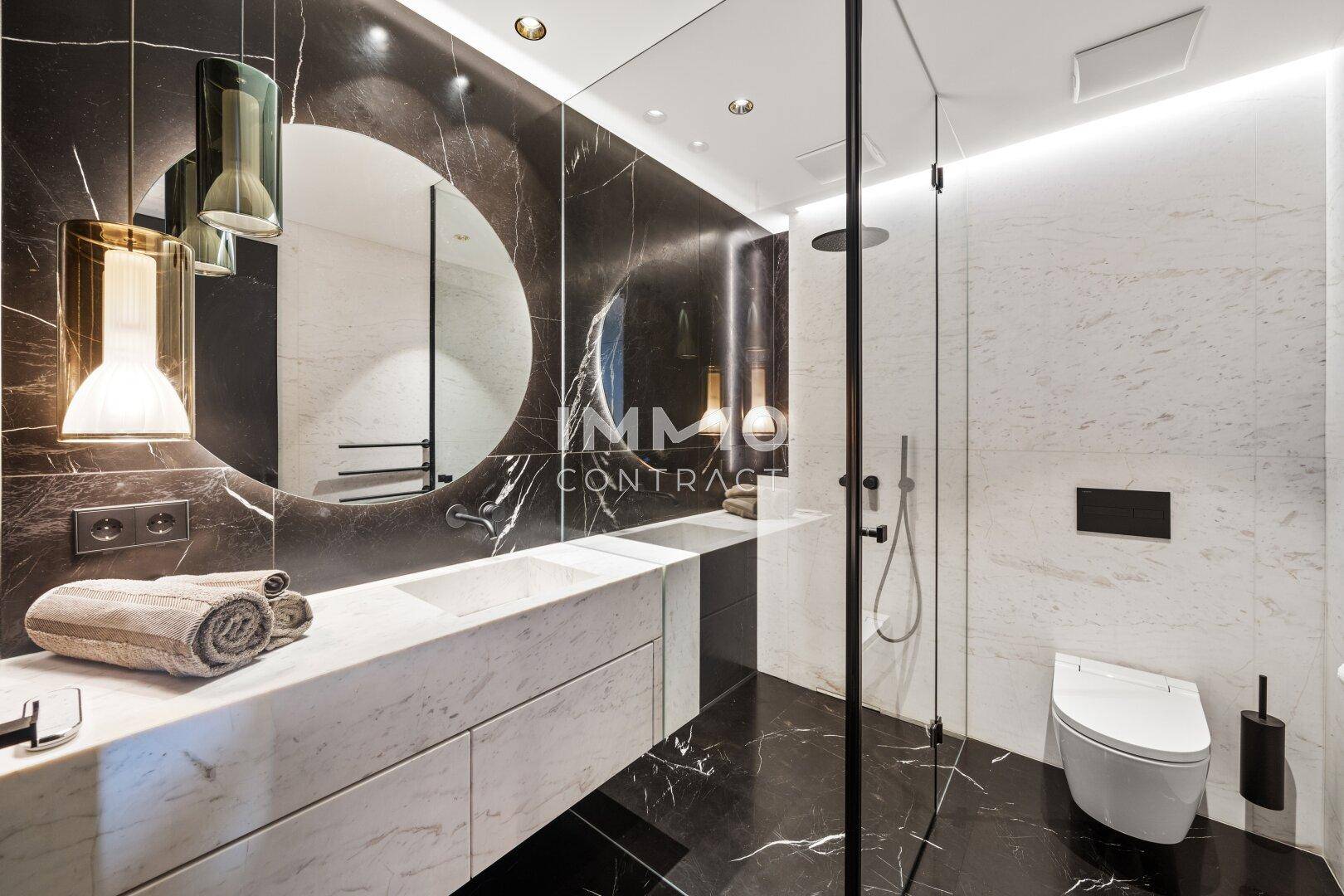 Luxuriöses Badezimmer mit dunklem Marmor, Doppelwaschbecken und begehbarer Dusche.