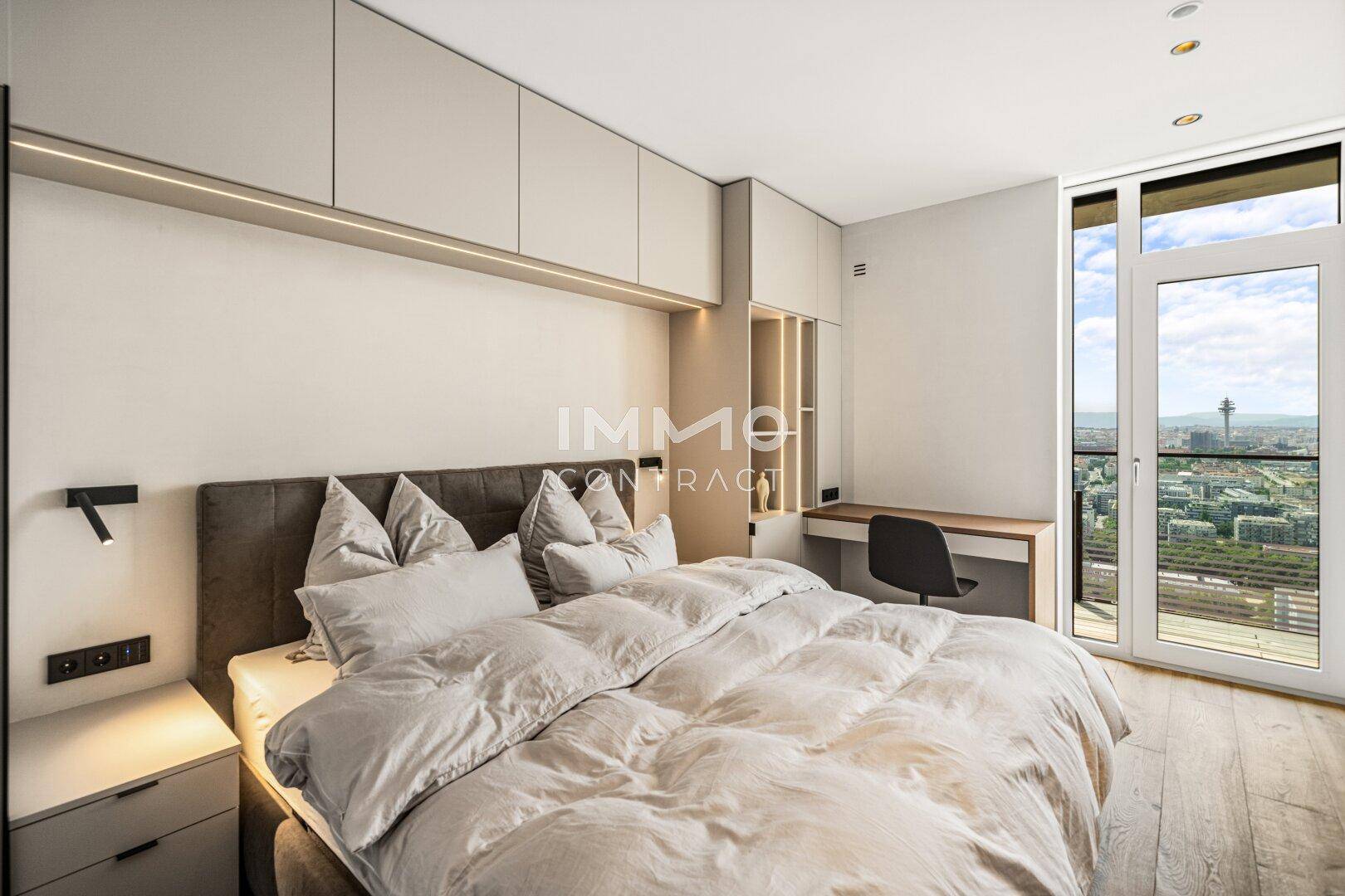 Schlafzimmer mit Einbauschränken, Schreibtisch und Zugang zu einem Balkon mit Stadtblick.