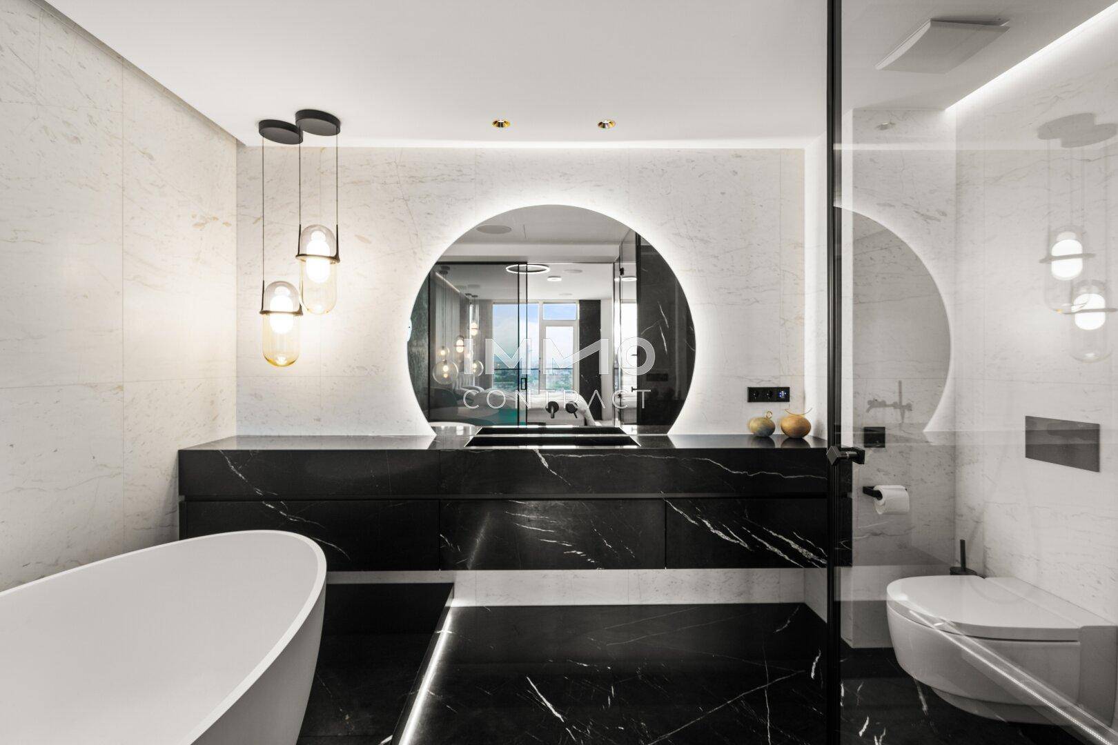 Elegantes Badezimmer mit freistehender Badewanne, schwarzem Marmor und beleuchtetem Spiegel.