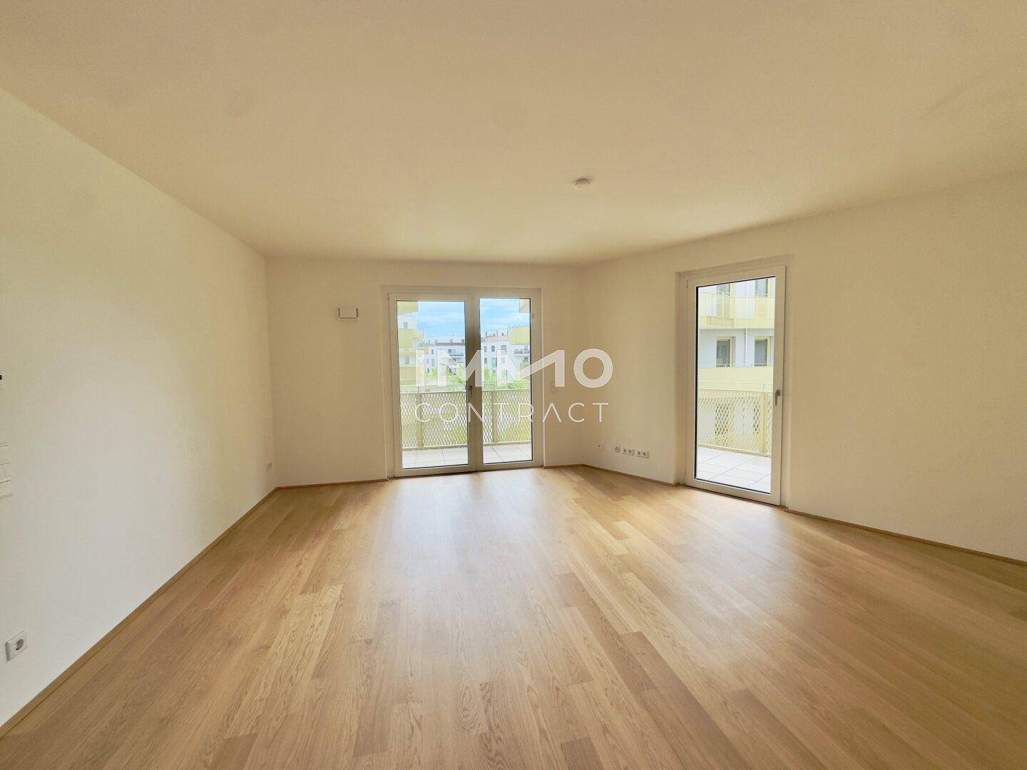 Geräumiges Wohnzimmer mit Parkettboden und großen Fenstern, die viel Tageslicht hereinlassen.