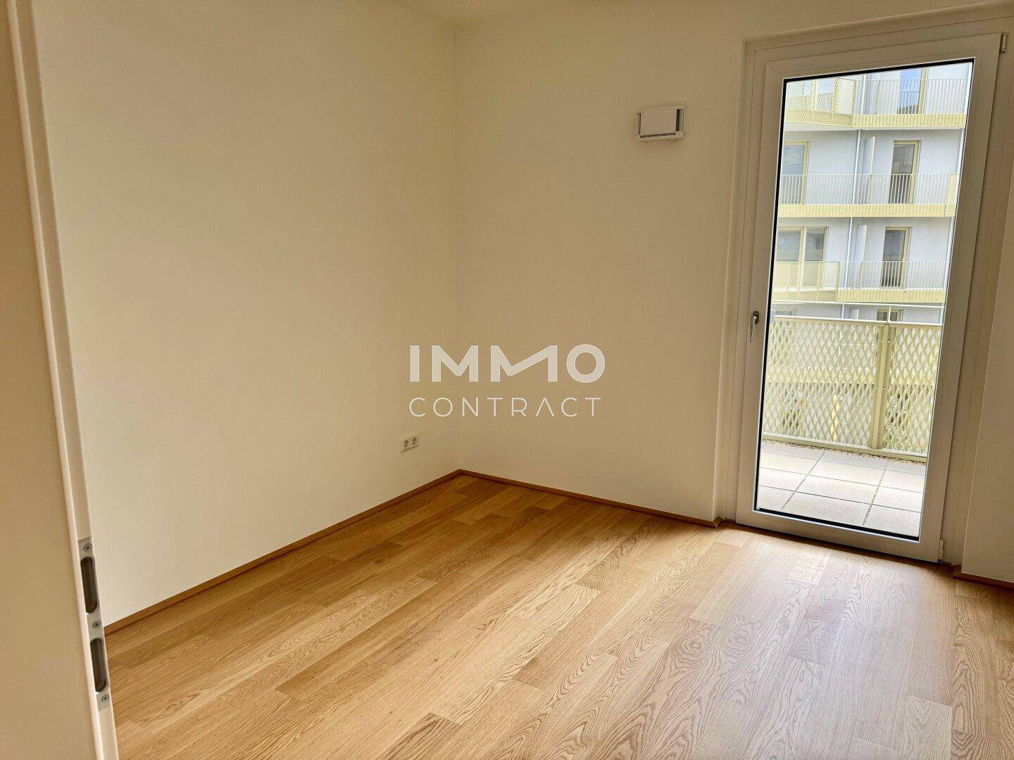 Leeres Zimmer mit hellem Parkettboden und Zugang zu einem Balkon, bereit zum Einrichten.