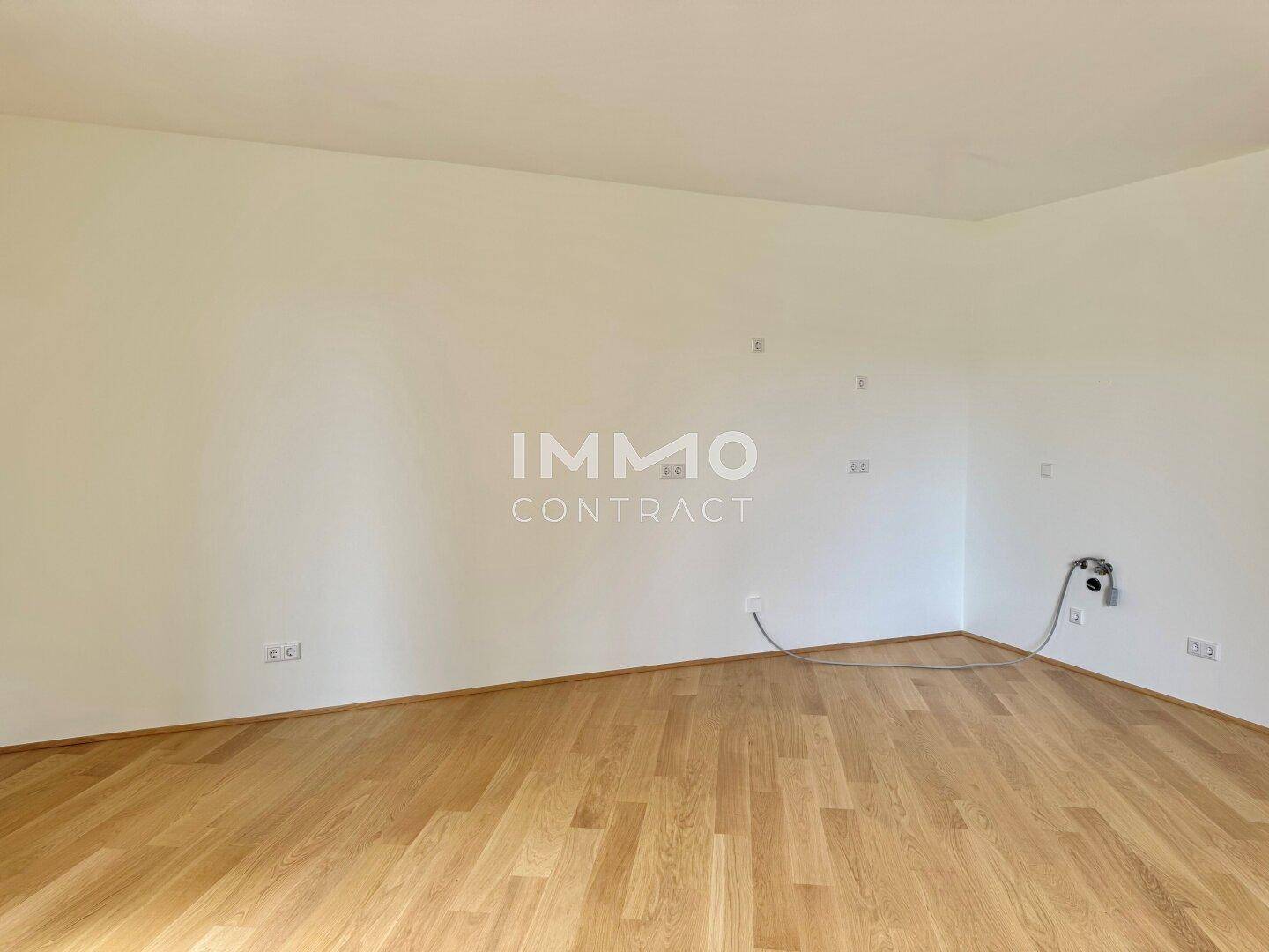 Leerer Küchenbereich mit Parkettboden und Anschlüssen für die Installation einer Einbauküche.