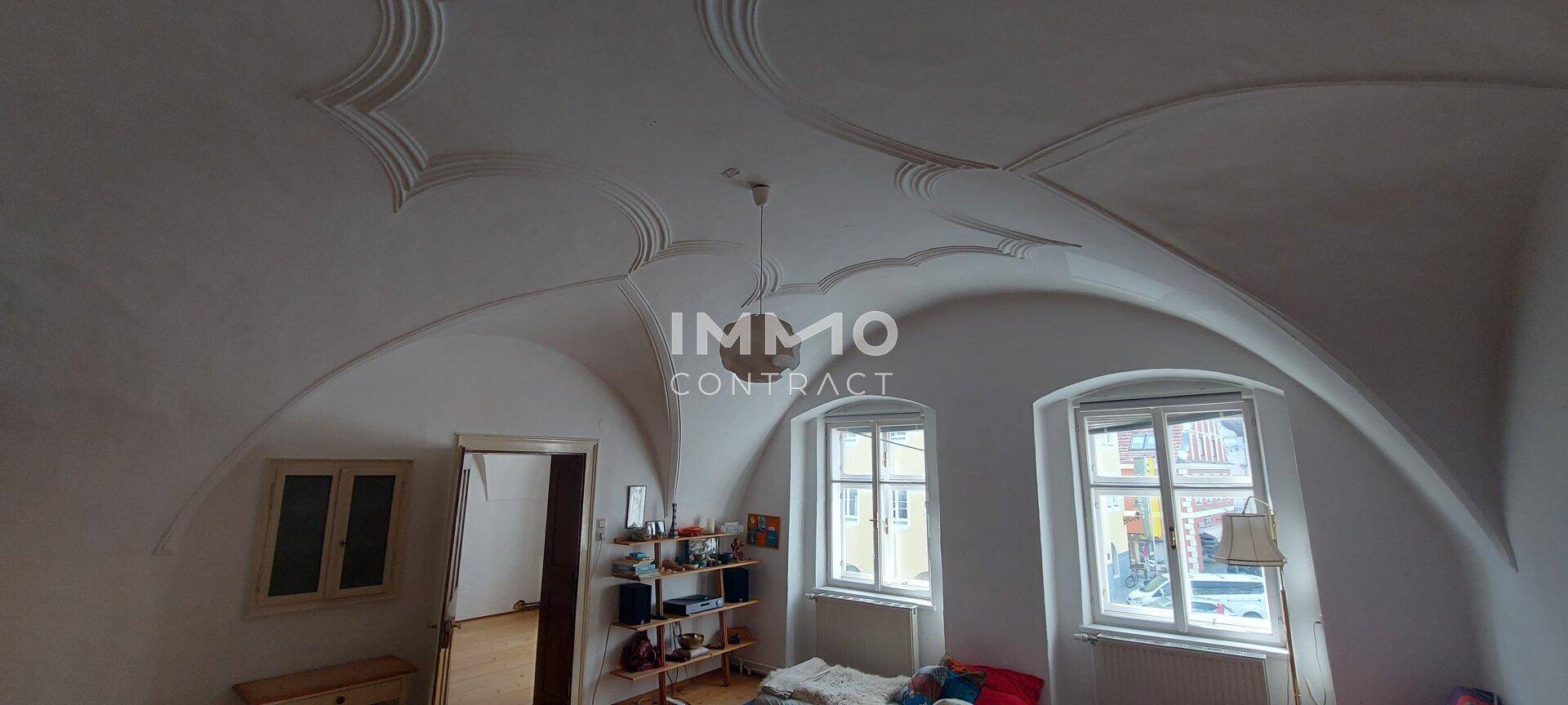Historisches Zimmer mit kunstvoll gewölbter Decke und zwei Fenstern, die Tageslicht hereinlassen.