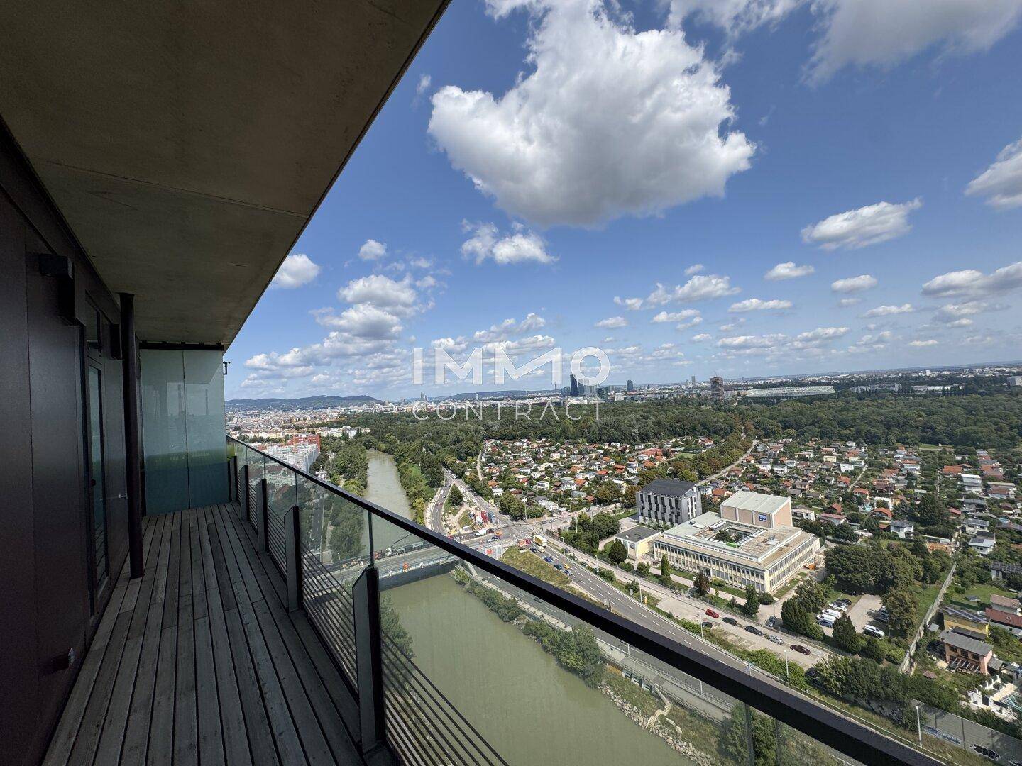 Geräumiger Balkon mit Holzboden und Glasgeländer bietet einen weiten Blick über die Stadt und den Fluss.
