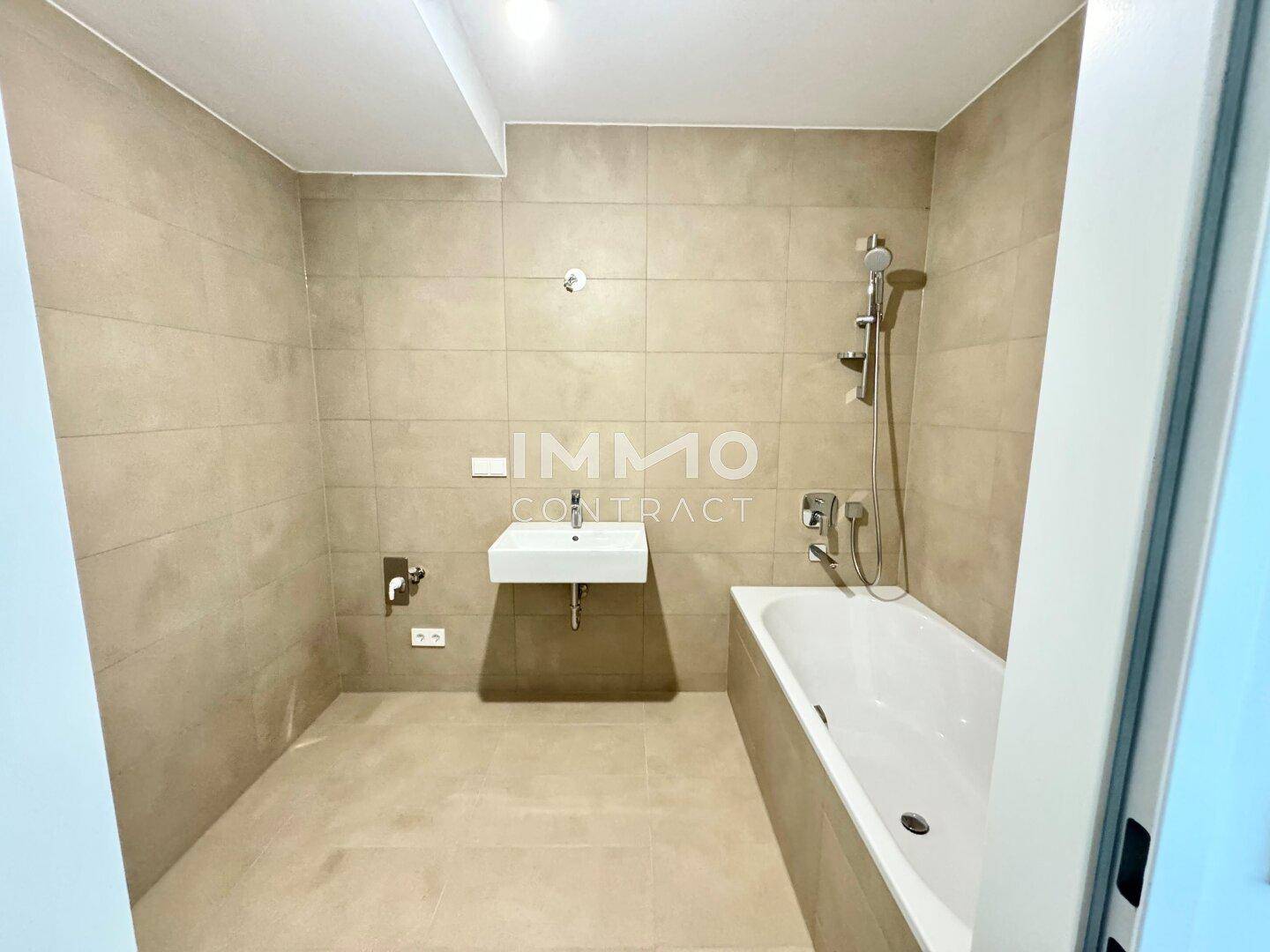 Modernes Badezimmer mit beigefarbenen Fliesen, Badewanne und einem einzelnen Waschbecken.