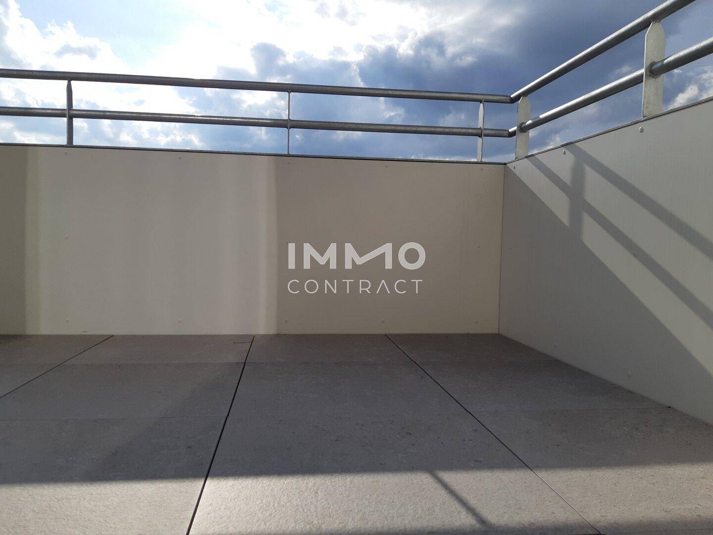 Leerer Balkon mit Fliesenboden und Metallgeländer unter bewölktem Himmel.
