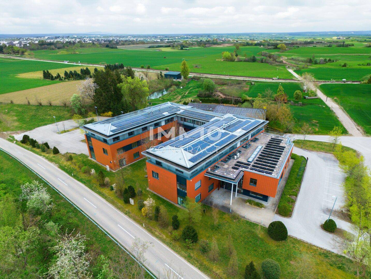 Weitläufige Luftaufnahme eines modernen Bürokomplexes mit Solaranlagen auf dem Dach, eingebettet in eine grüne Landschaft.