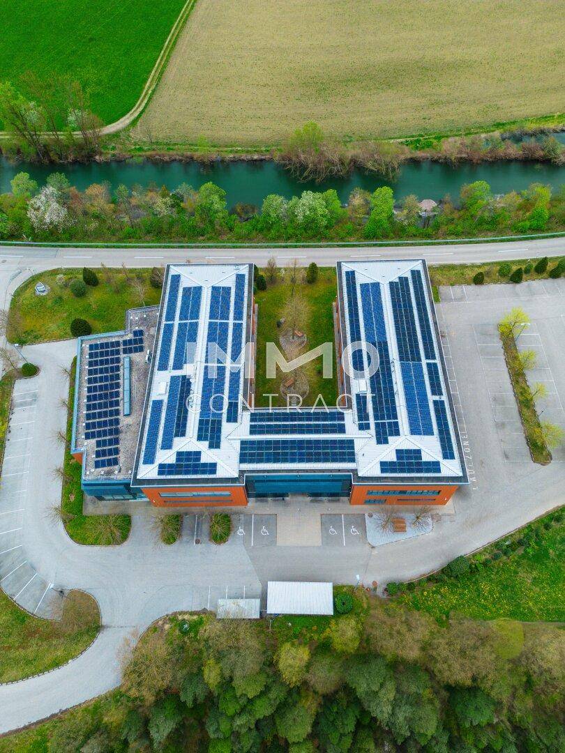 Direkte Draufsicht auf ein modernes Bürogebäude mit symmetrisch angeordneten Solarmodulen auf dem Dach, neben einem Fluss.