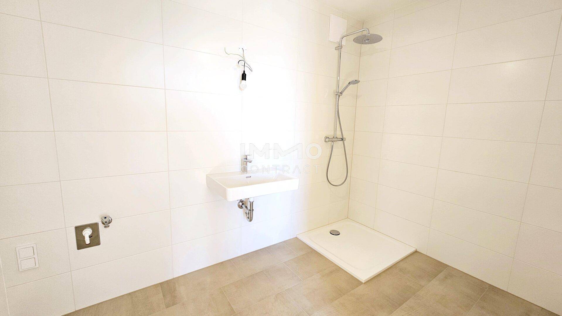 Modernes Badezimmer mit weißen Fliesen, ebenerdiger Dusche und Einzelwaschbecken.