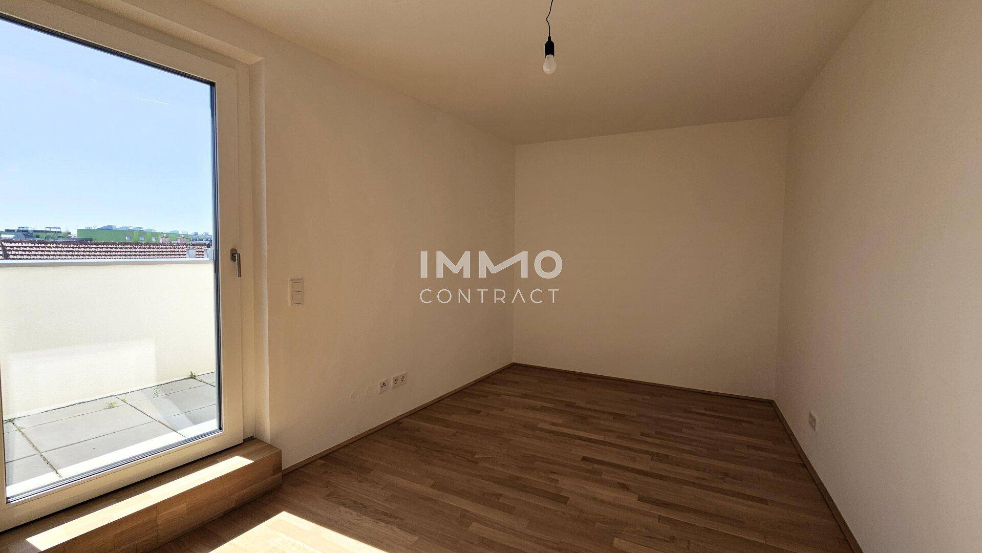 Schlafzimmer mit Holzboden und großem Fenster, das viel Tageslicht hereinlässt.