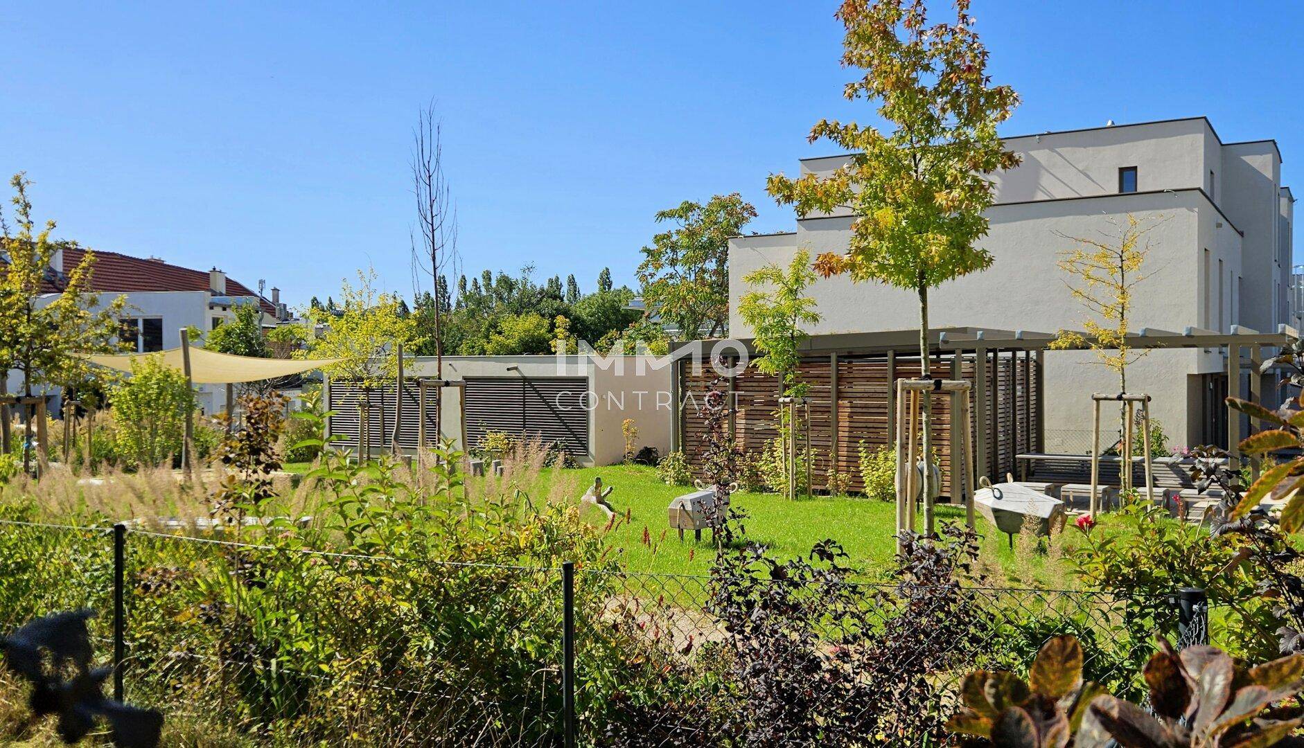 Weitläufige Gemeinschaftsgartenanlage mit Bäumen und Sitzgelegenheiten zwischen modernen Gebäuden.