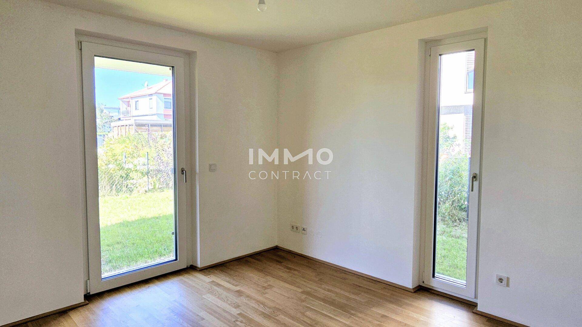 Freundliches Zimmer mit Parkettboden und zwei großen Fenstern mit Blick ins Grüne.