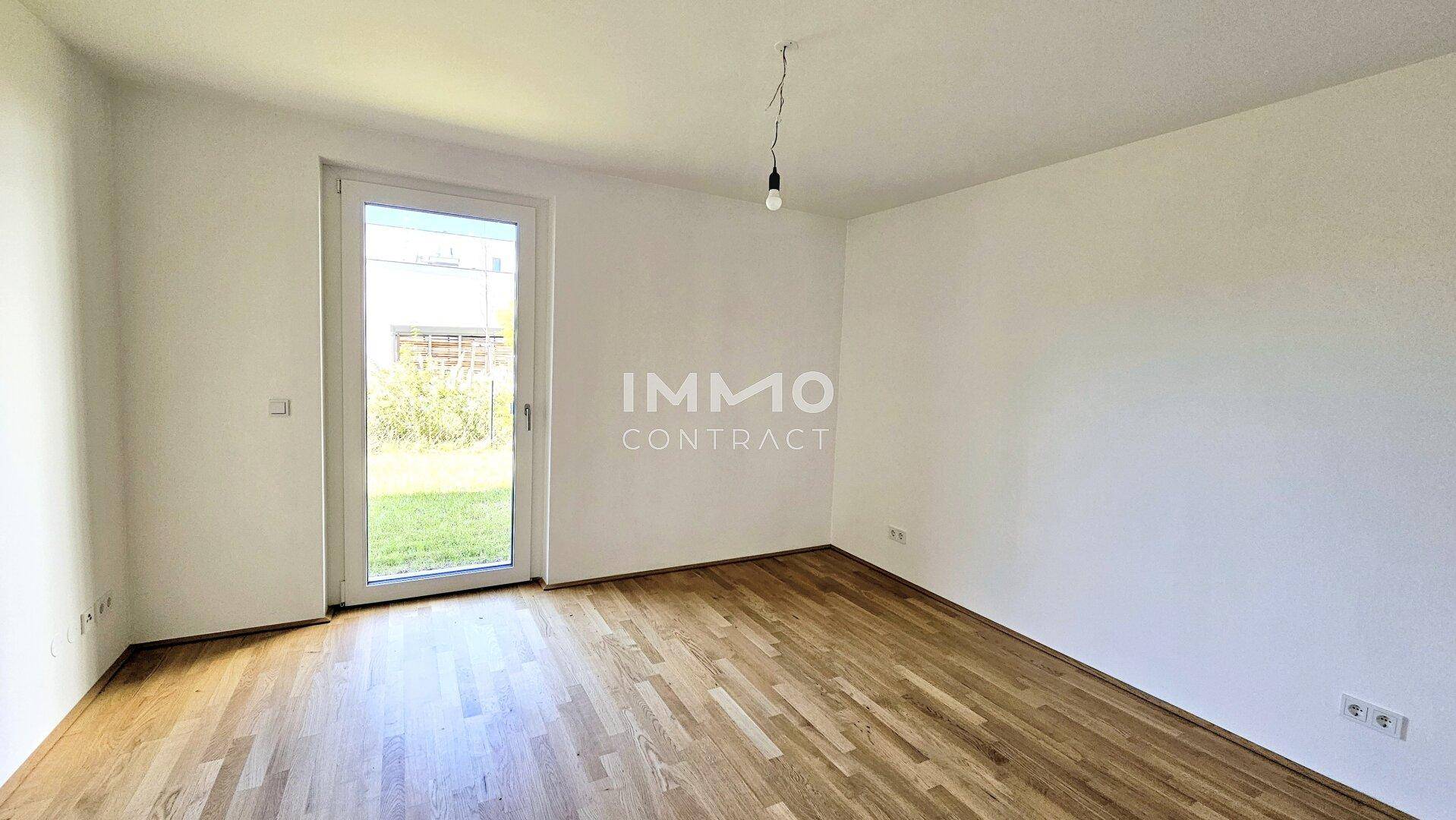 Geräumiges Zimmer mit Parkettboden und direktem Zugang zur Grünfläche im Freien.