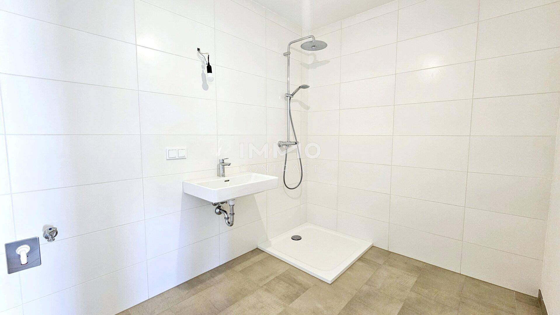 Modernes Badezimmer mit weißen Fliesen, ebenerdiger Dusche und einem einzelnen Waschbecken.