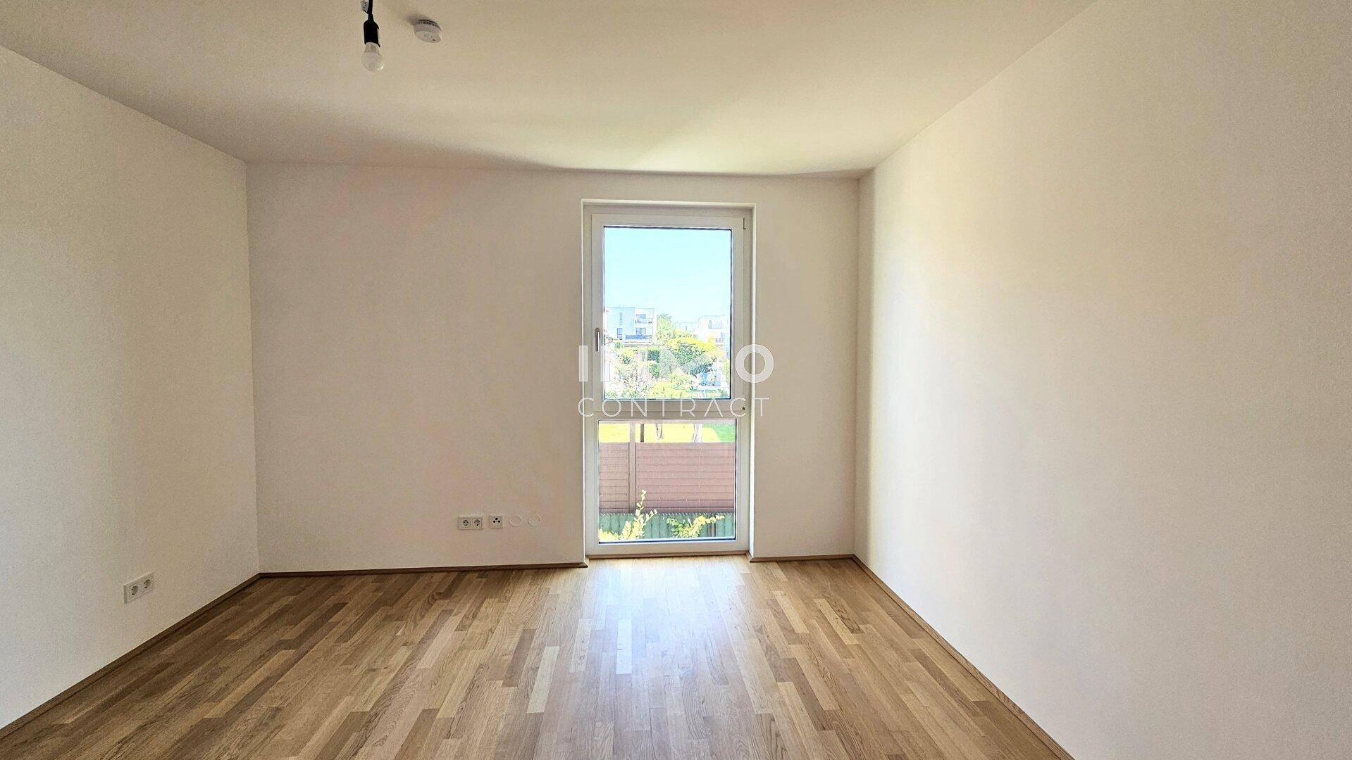 Helles Schlafzimmer mit Parkettboden und Fenster mit Blick auf die grüne Umgebung.