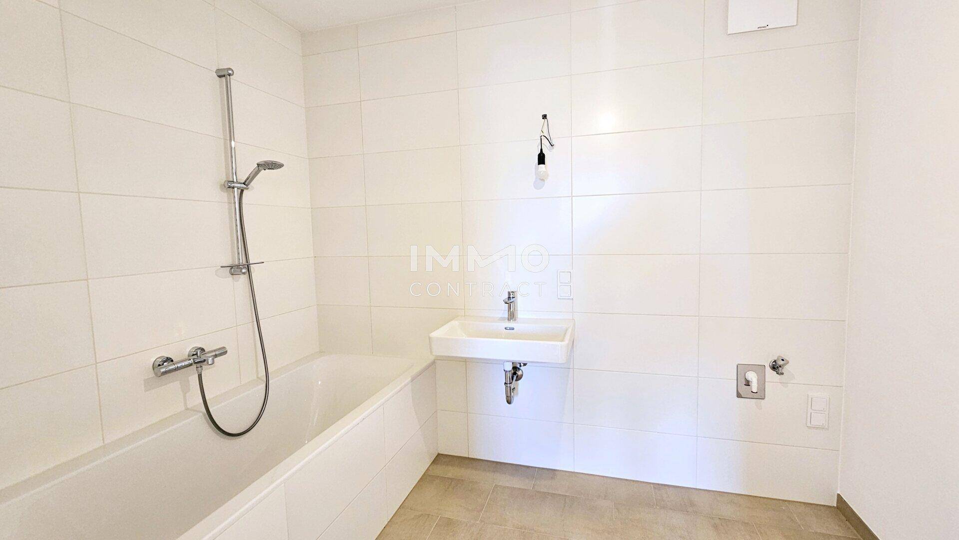 Modernes Badezimmer mit weißen Wandfliesen, Badewanne mit Duschfunktion und Waschbecken.