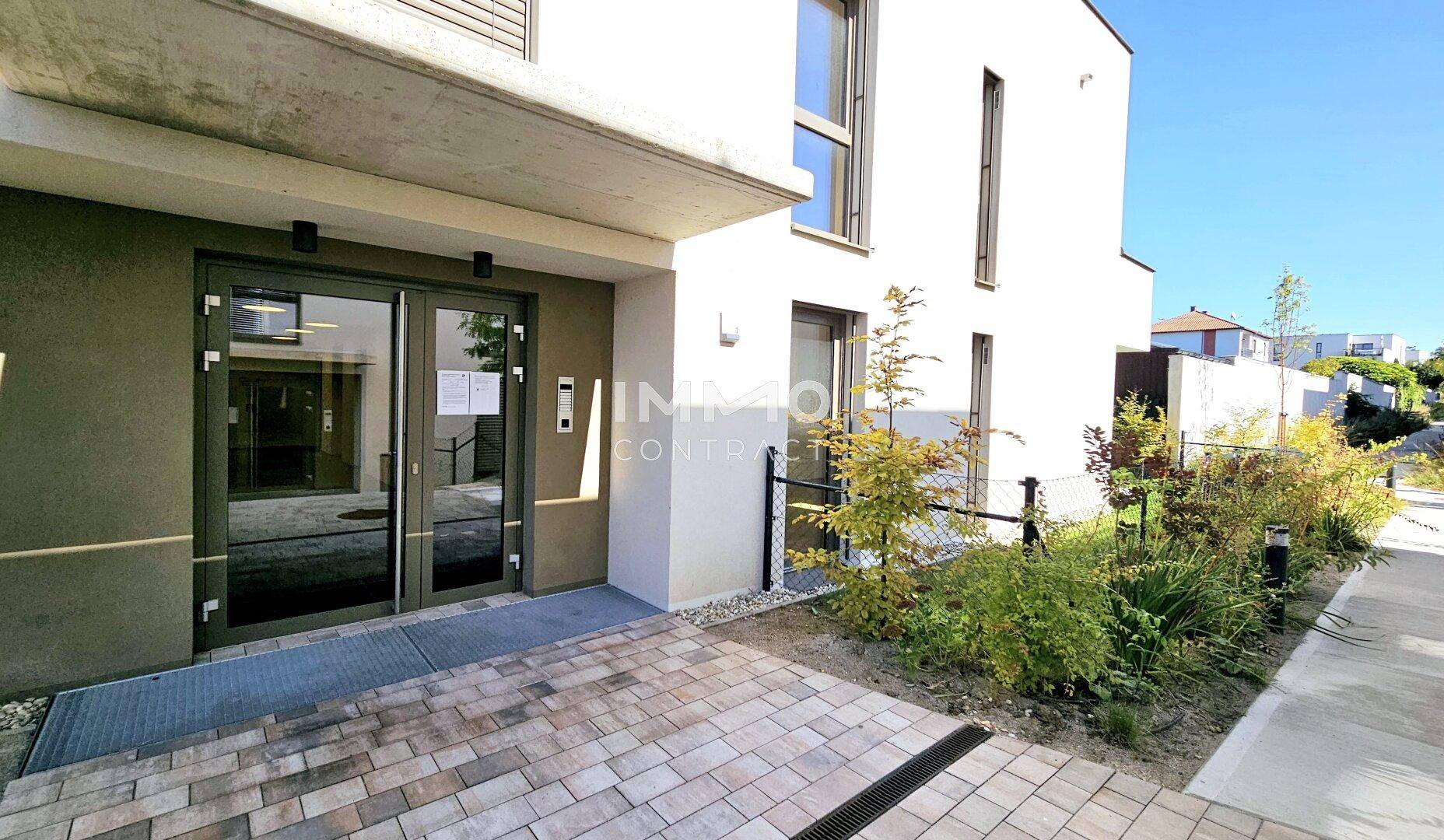 Moderner Eingangsbereich des Wohngebäudes mit Glasportal und gepflegter Außenanlage.