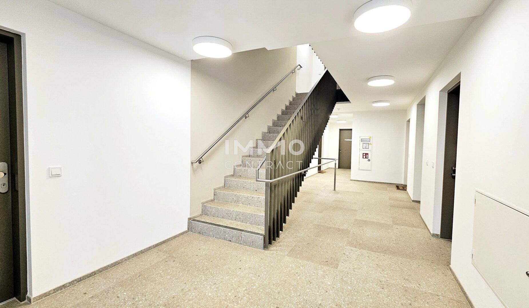 Heller Treppenaufgang im modernen Wohngebäude mit Steinfliesen und robustem Metallgeländer.