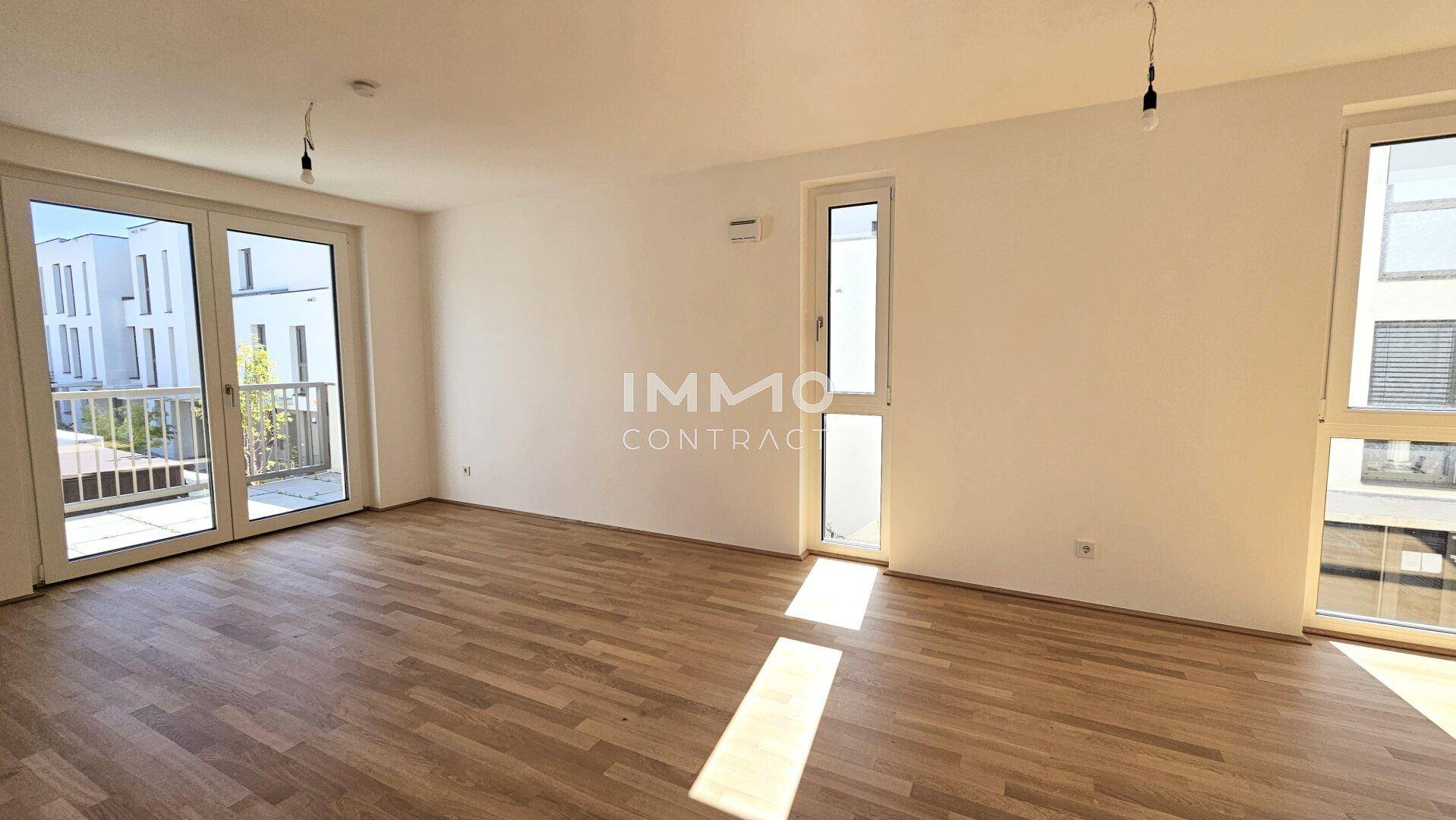Helles, unmöbliertes Wohnzimmer mit Parkettboden und Zugang zu einem Balkon.