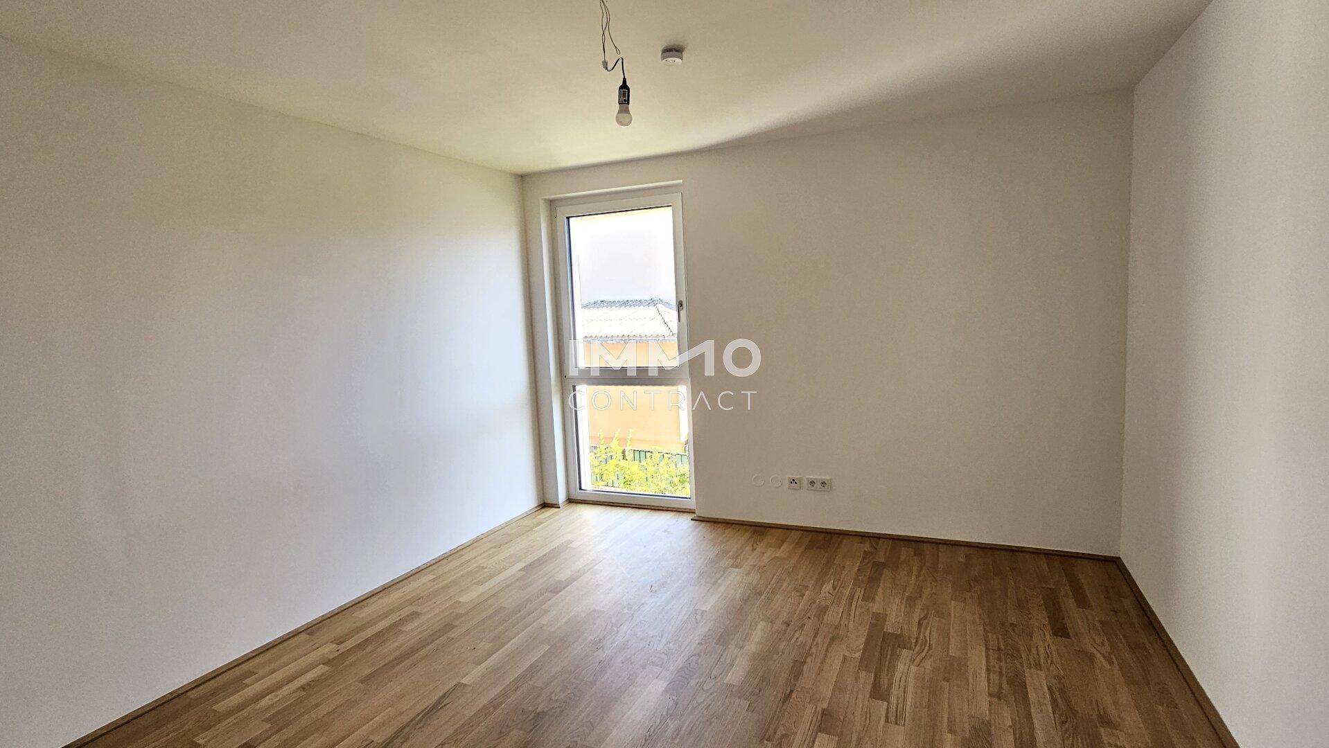 Unmöbliertes Schlafzimmer mit hellem Parkettboden und großem Fenster für viel Tageslicht.
