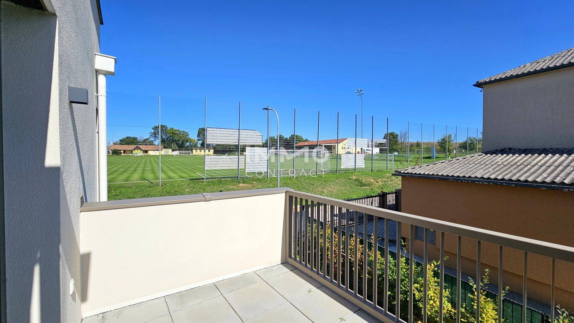 Balkon mit Fliesenboden und Blick auf einen Sportplatz und die grüne Umgebung.