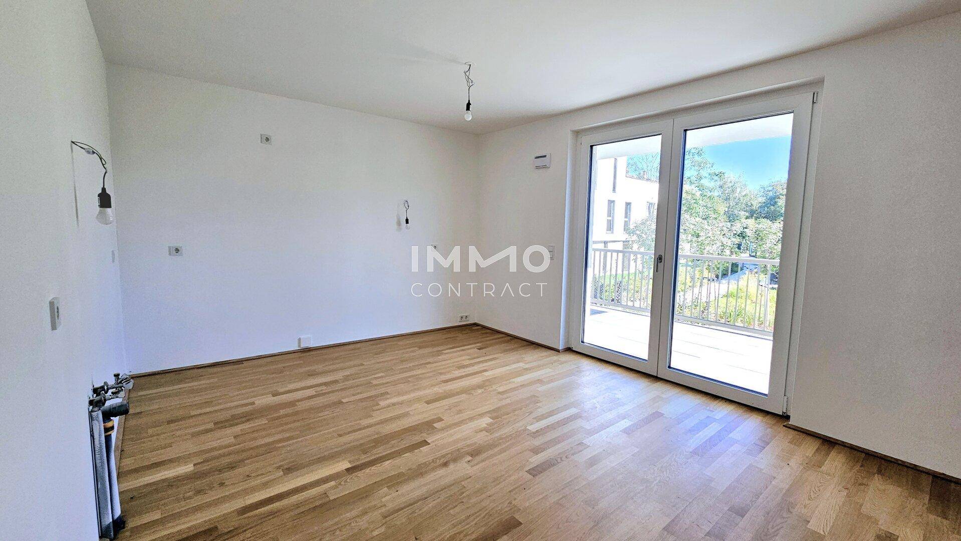 Unmöbliertes Wohnzimmer mit hellem Parkettboden und direktem Balkonzugang.