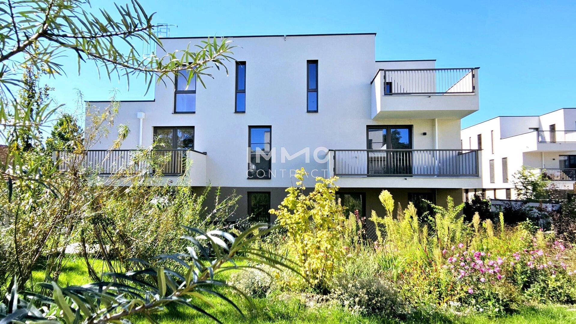 Moderne Wohnanlage mit weißer Fassade und üppigem, grünem Gartenbereich.