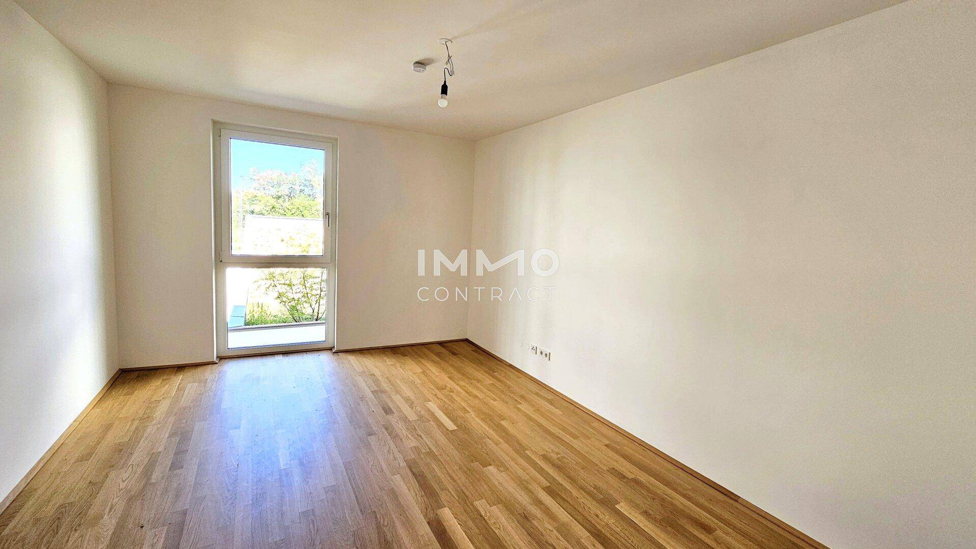 Helles Schlafzimmer mit Parkettboden und einem großen Fenster mit Blick ins Grüne.
