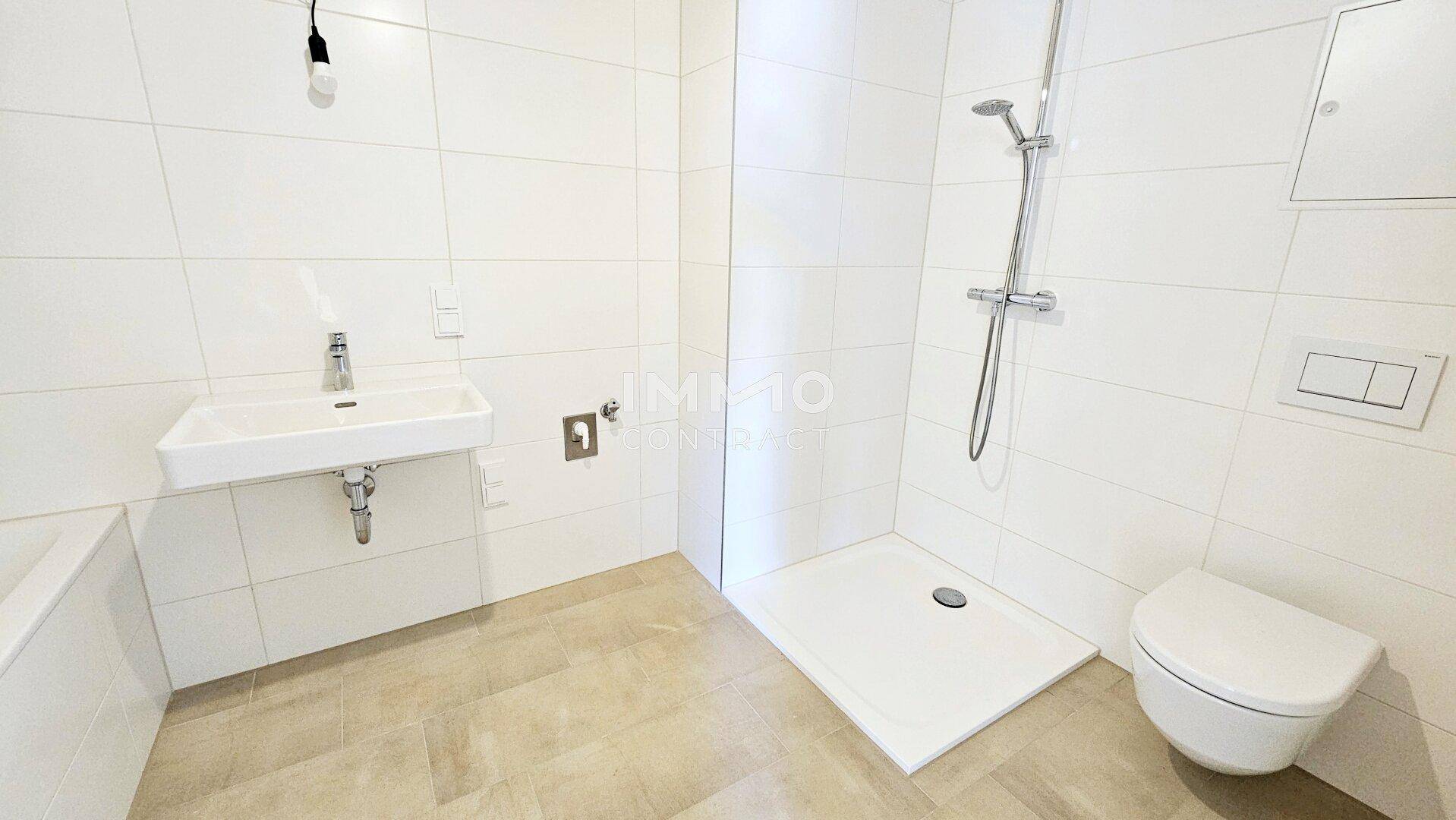 Modernes Badezimmer mit weißen Fliesen, ebenerdiger Dusche und wandhängendem WC.