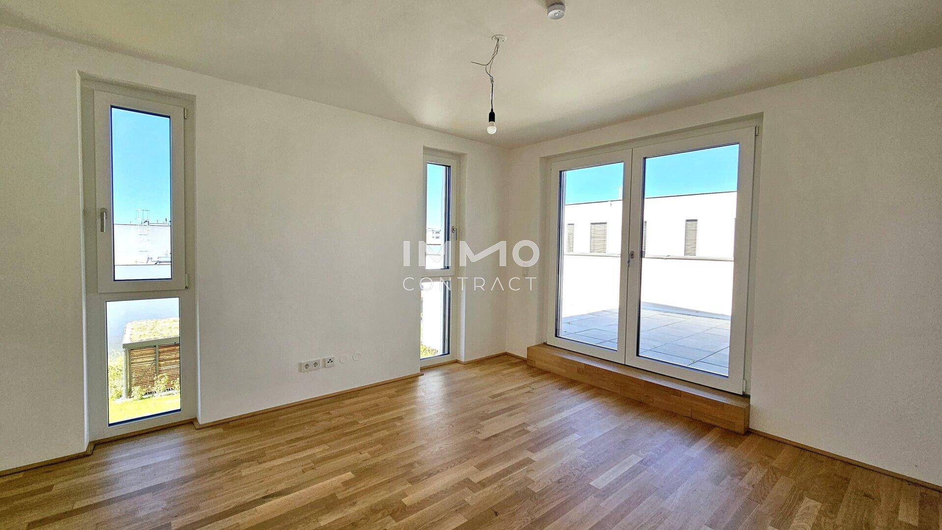 Helles Zimmer mit Parkettboden, großen Fenstern und direktem Zugang zu einer Außenterrasse.