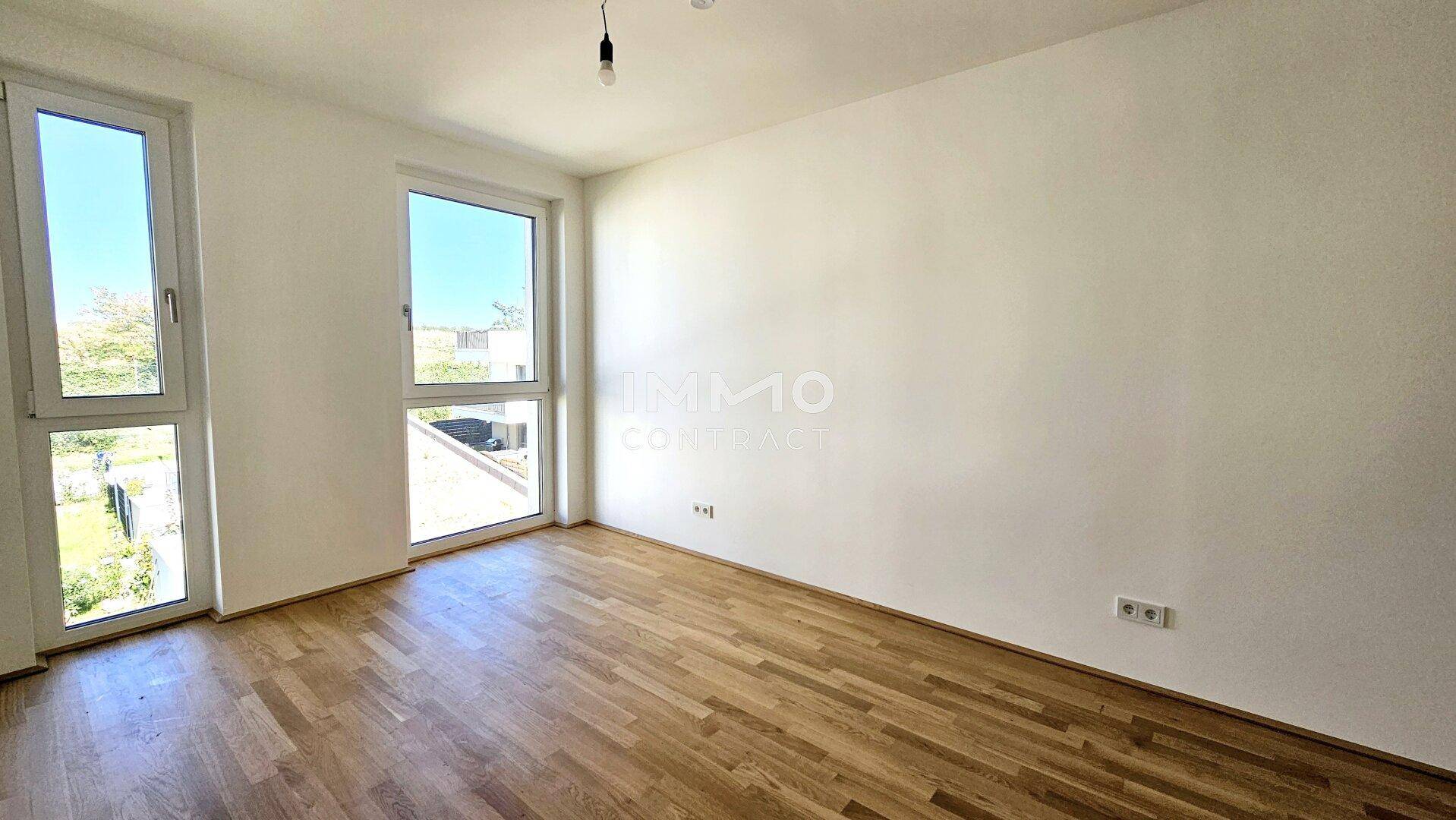 Geräumiges Zimmer mit Holzparkett und hohen Fenstern, die einen Blick ins Grüne bieten.