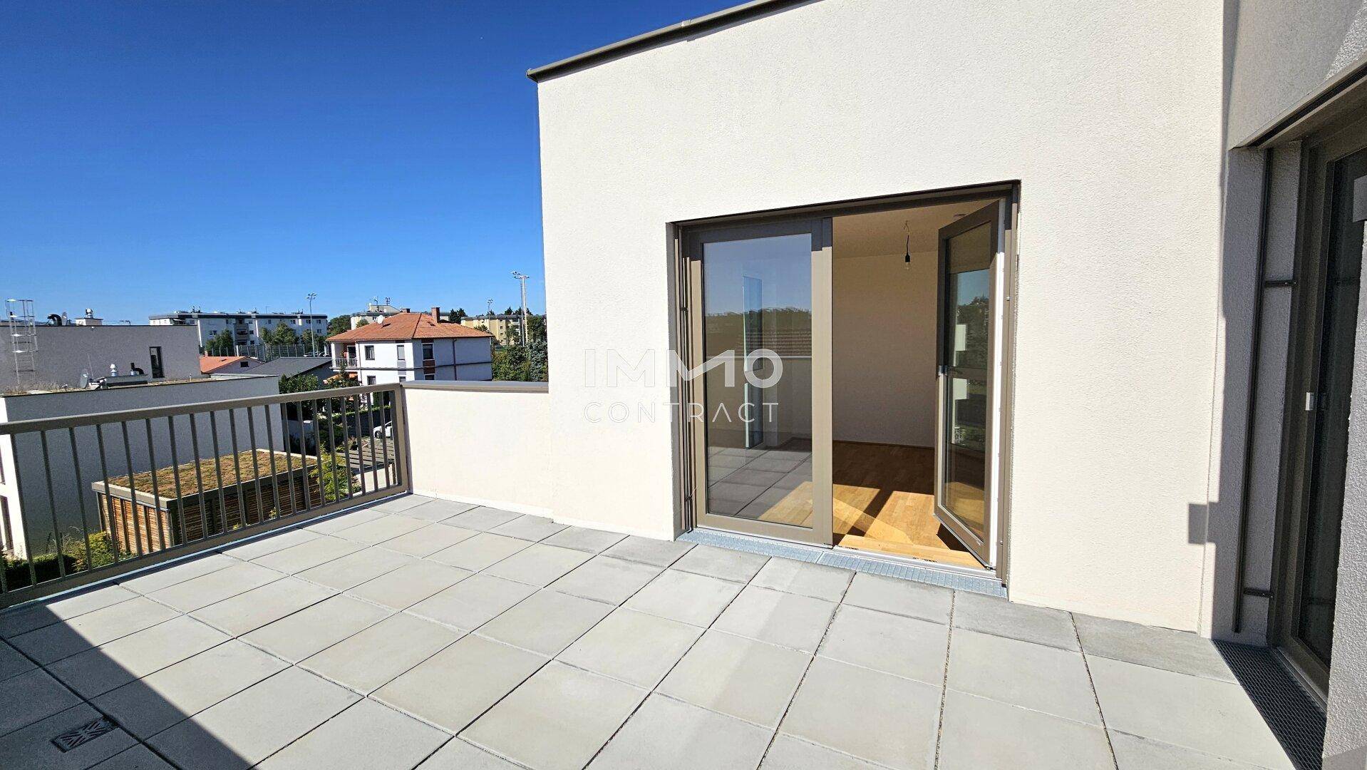 Sonnige Terrasse mit Fliesenboden und Blick in einen hellen Innenraum durch eine Glastür.