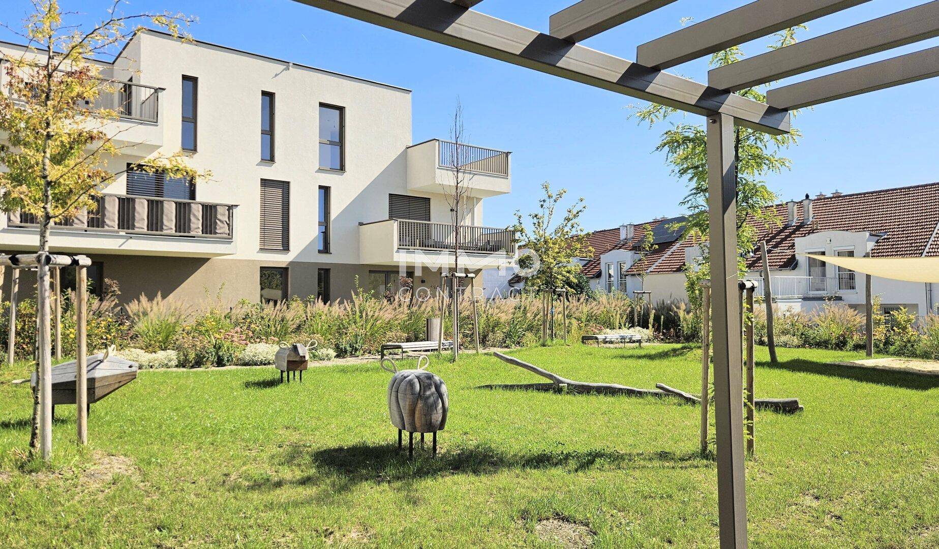 Gepflegter Gemeinschaftsgarten mit Rasenflächen, Spielgeräten und moderner Wohnbebauung im Hintergrund.