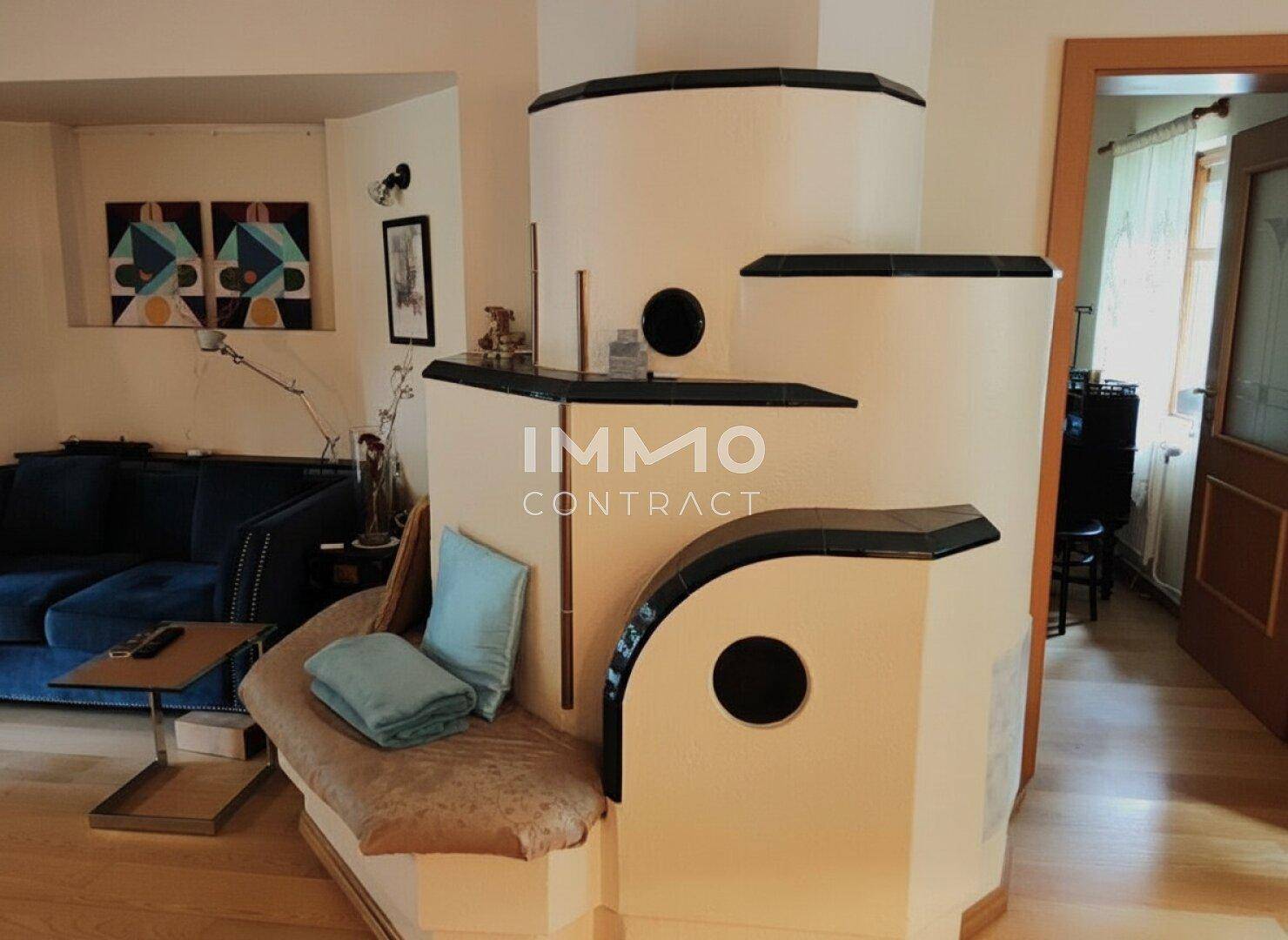 Wohnzimmer mit einem traditionellen Kachelofen, der Wärme spendet, und einem bequemen blauen Sofa im Hintergrund.