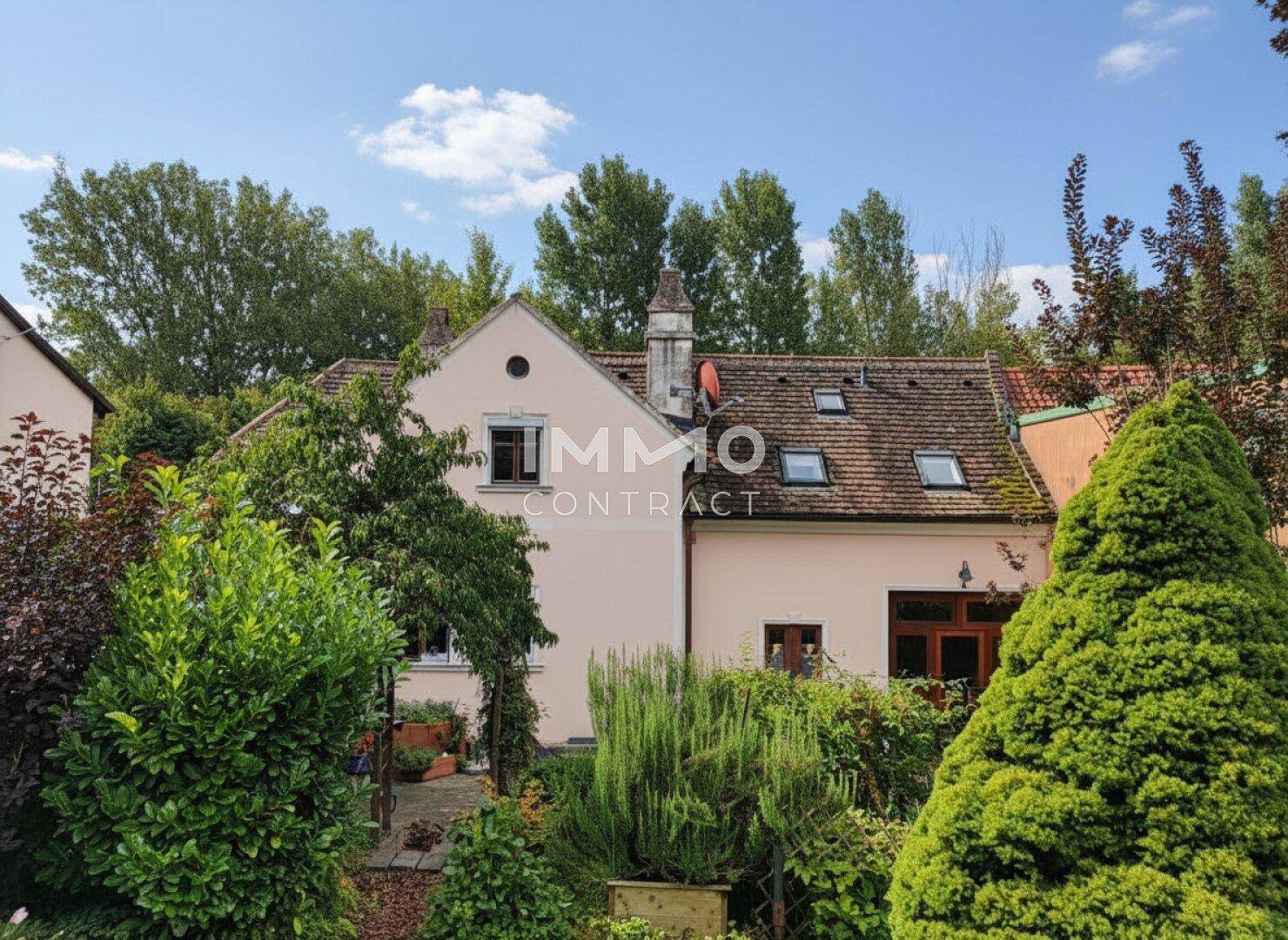 Rückansicht des Hauses mit Dachfenstern und einem gepflegten Garten mit verschiedenen Sträuchern und Bäumen.