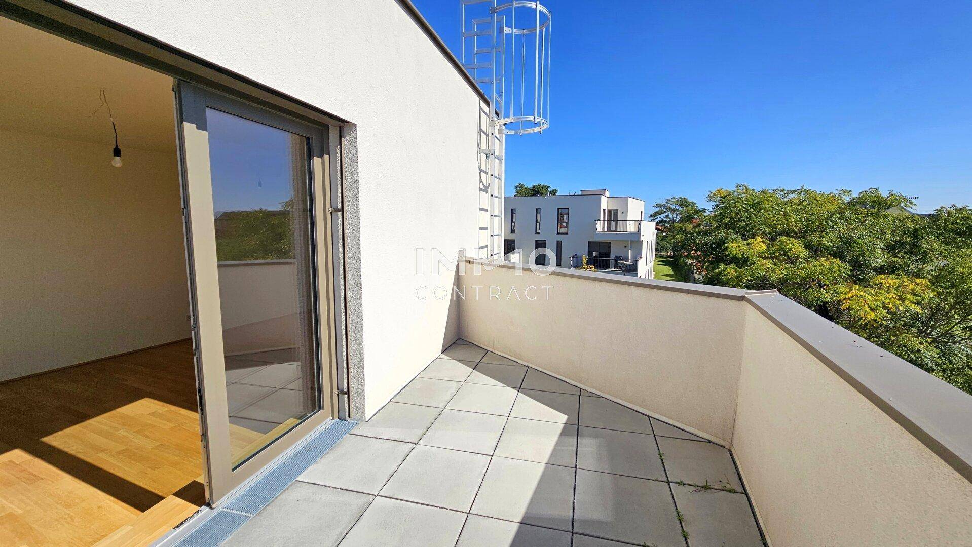 Sonniger Terrassenbereich mit Fliesenboden, Brüstung und Blick ins Grüne.