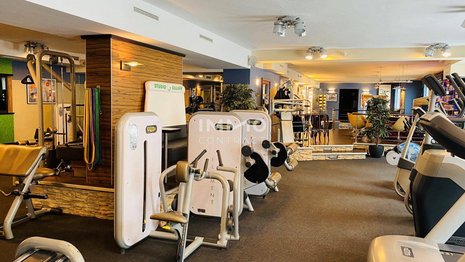 Geräumiger Fitnessraum mit einer Vielzahl moderner Trainingsgeräte und einem gemütlichen Loungebereich im Hintergrund.