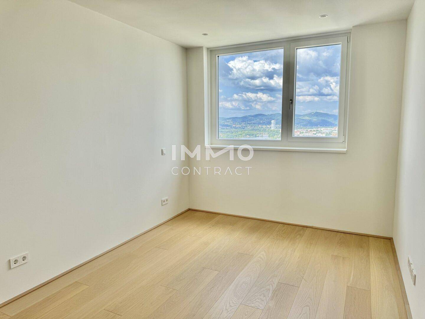 Helles Schlafzimmer mit Parkettboden und Fenster, das einen weiten Blick auf die Landschaft bietet.