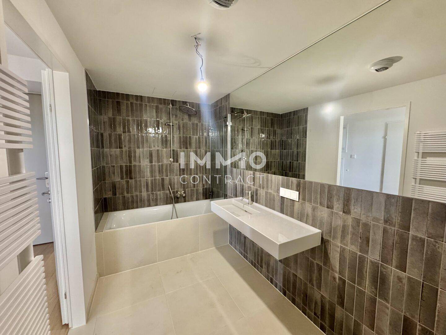 Modernes Badezimmer mit Badewanne, Einzelwaschbecken und großen Wandspiegeln.