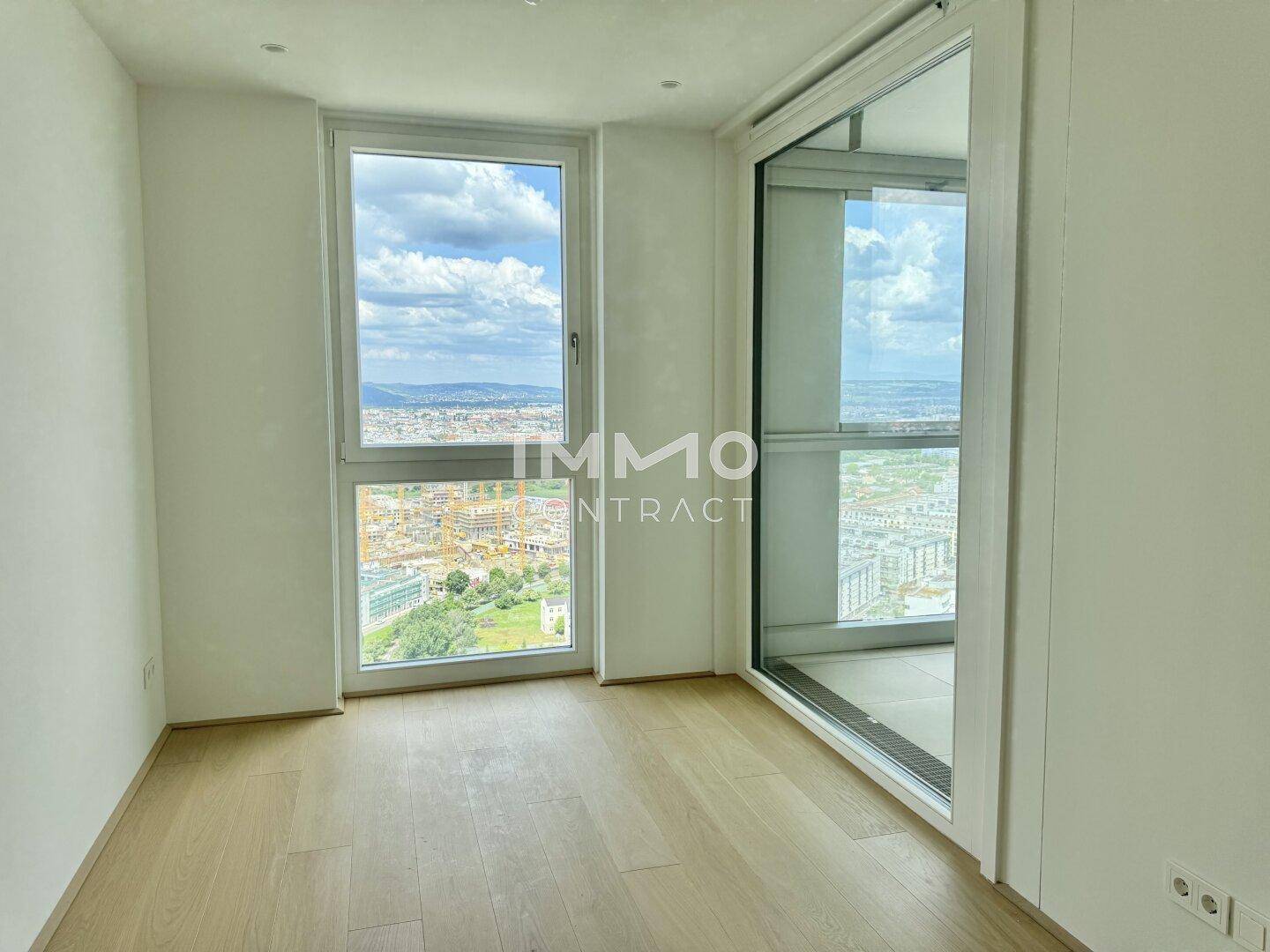 Lichtdurchflutetes Zimmer mit Holzboden und großen Fenstern, die einen Panoramablick ermöglichen.