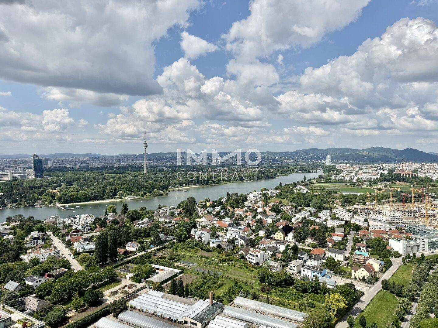 Weitläufiger Blick über die Stadt, die Donau und die umliegende grüne Landschaft unter blauem Himmel.
