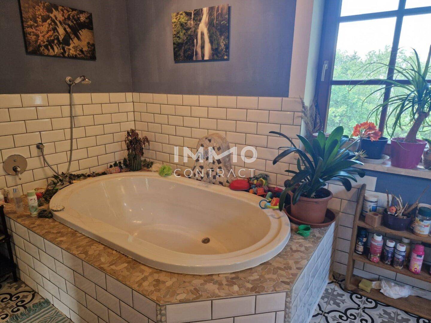 Badezimmer mit großer Badewanne, weißen Fliesen und Fenster mit Blick ins Grüne.