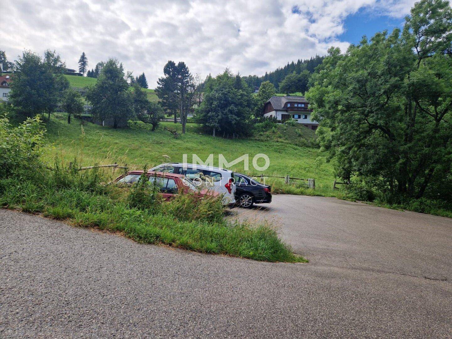Außenparkplatz mit mehreren Fahrzeugen, umgeben von grünen Wiesen und Bäumen.