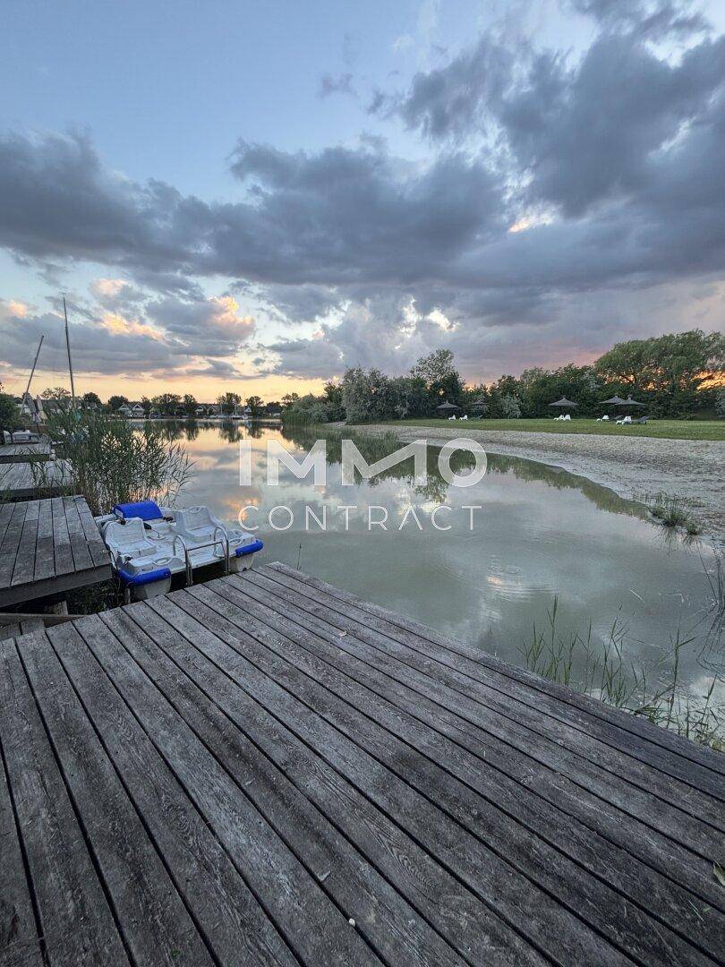 Holzsteg am Seeufer mit einem kleinen Boot und malerischem Sonnenuntergangshimmel.