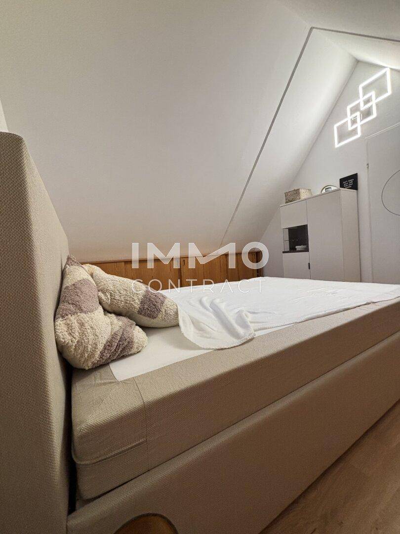 Helles Schlafzimmer im Dachgeschoss mit schräger Decke, Holzboden und modernem Bett.