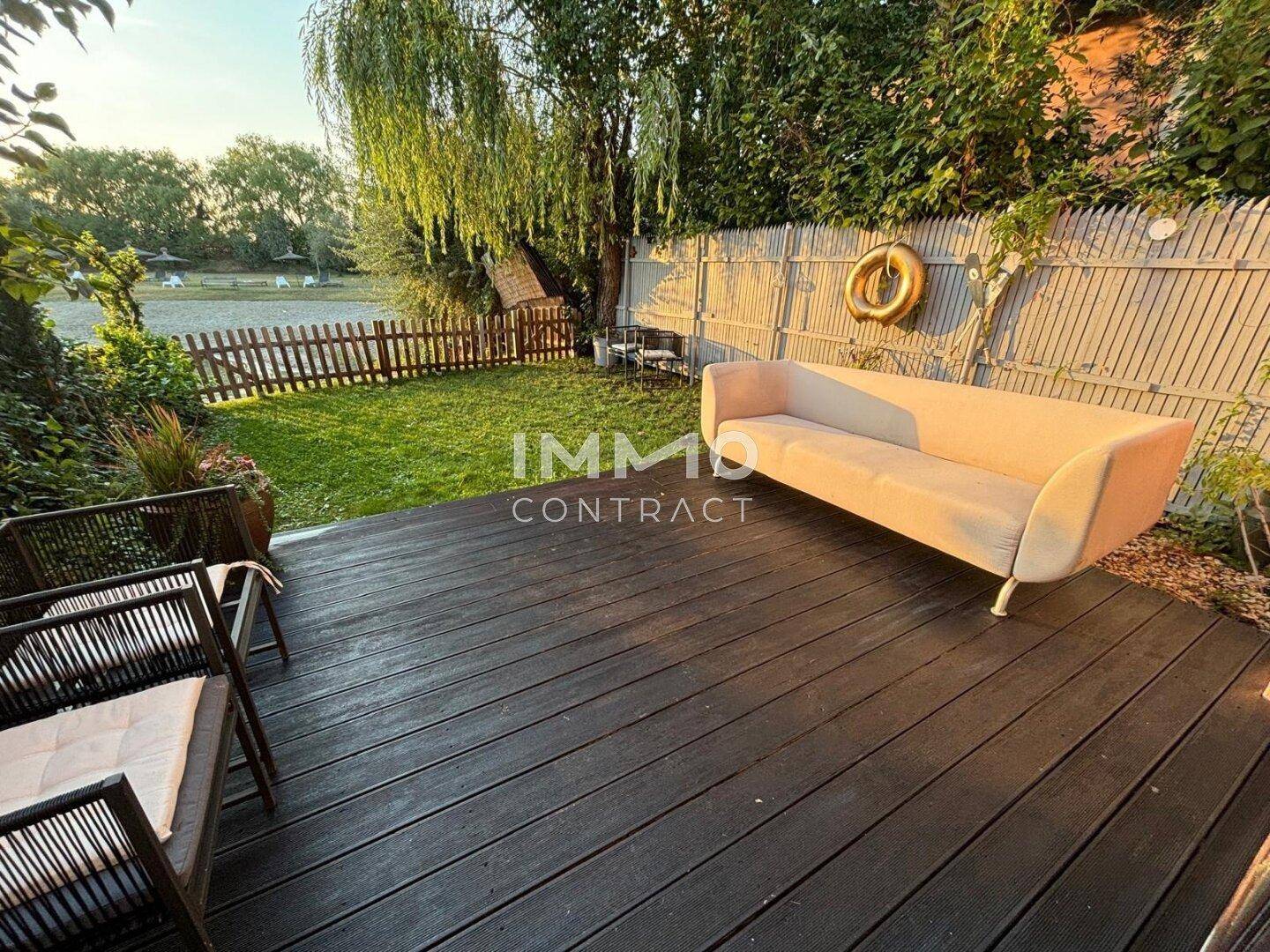 Gemütliche Holzterrasse mit bequemen Gartenmöbeln und Blick auf den See.