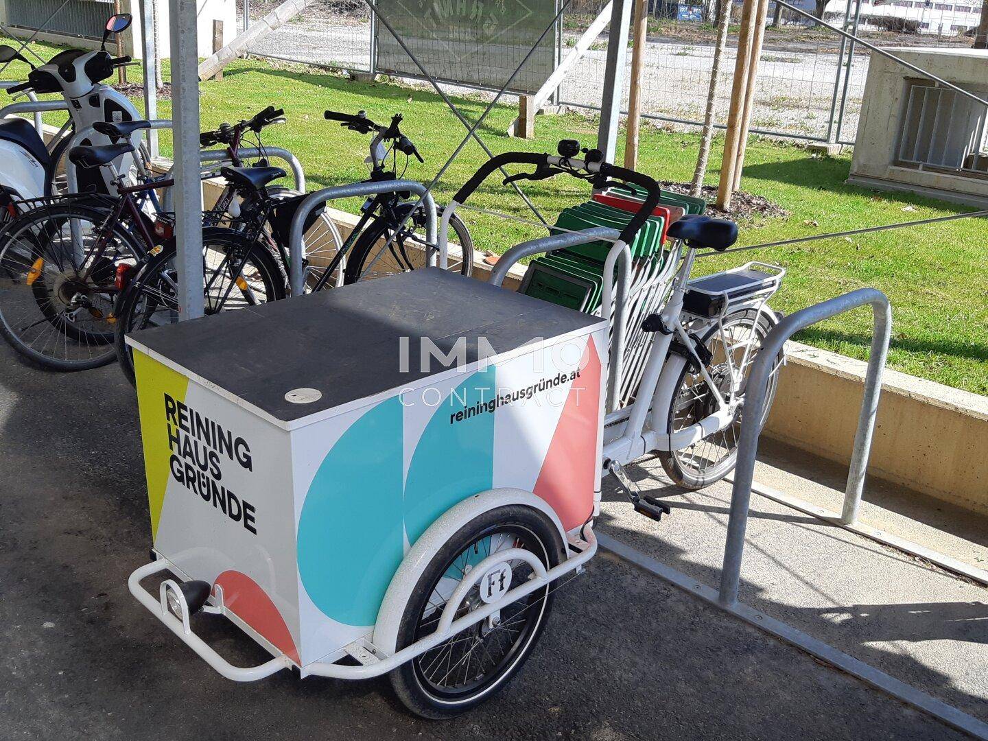 Ein Lastenfahrrad steht in einem Fahrradständer im Freien, umgeben von weiteren Fahrrädern.