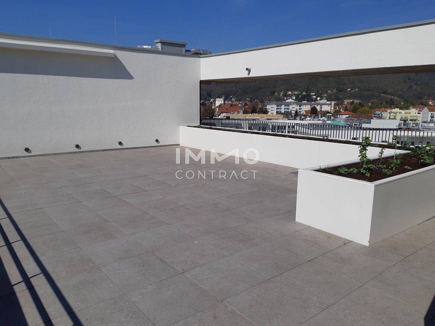 Großzügige Dachterrasse mit Fliesenboden und Pflanzkübeln, bietet weite Ausblicke über die Stadt.